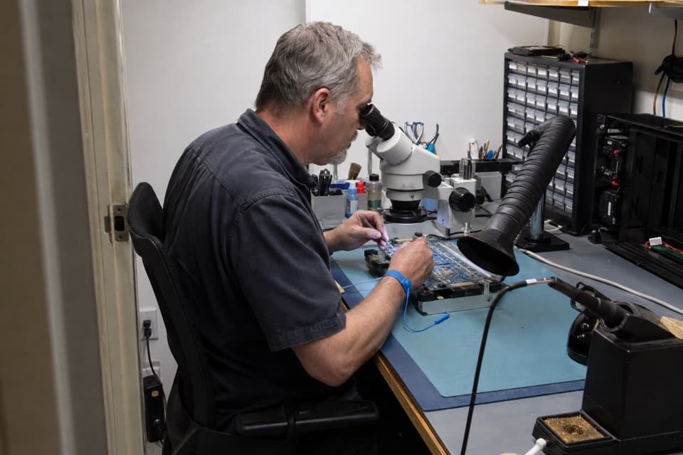 Illustrative scene of a repair technician examining a circuit board under a microscope